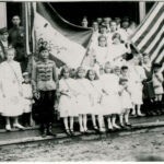 YMCA 1922 Monaville, WV. Hungarian Flag Day. Lena Loslo is holding the flag. Helen Tarkany Piros is the 2nd girl to the right of the man in uniform (his name maybe Berti). On the right, the little boy wearing the Russian looking hat is John Haslam. Courtesy of Bob Piros. Monaville, WV YMCA Flag Day, 1922