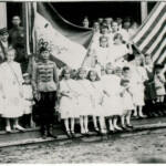YMCA 1922 Monaville, WV. Hungarian Flag Day. Lena Loslo is holding the flag. Helen Tarkany Piros is the 2nd girl to the right of the man in uniform (his name maybe Berti). On the right, the little boy wearing the Russian looking hat is John Haslam. Courtesy of Bob Piros. Monaville, WV YMCA Flag Day, 1922