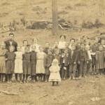 Picture of Principal Garnett O. Nelson with teachers and students courtesy of Brenna Mitchell.
From his obit. Garnett was born at Simoda. His parents were Joseph W. Nelson and Martha A. Hedrick. He was the principal of a grade school and listed his employer as the Logan County Board of Education when he registered for the draft. Garnett registered on 24 May 1917 in Logan County, WV.
That death leaves a shining mark was said long ago and has been demonstrated over and over. But perhaps never more strikingly so than in the subject of this sketch. Garnett Otis Nelson was born June 21, 1890. Entrained for Camp Lee May 25, 1918, and died November 15, 1918. In Camp Lee he was promoted to office of Corporal and in France he became a Sergeant.
In 1907 he completed the free school course, then taught in his home county of Pendleton four years, completed the state normal course at Shepherd College in the class of 1914. Later he attended the West Virginia University and taught in Logan County four years; one year as principal of the Henlawson school and three years as principal of Logan city school. Garnett Otis Nelson Postcard photo with teachers and students
