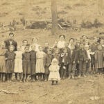 Picture of Principal Garnett O. Nelson with teachers and students courtesy of Brenna Mitchell.
From his obit. Garnett was born at Simoda. His parents were Joseph W. Nelson and Martha A. Hedrick. He was the principal of a grade school and listed his employer as the Logan County Board of Education when he registered for the draft. Garnett registered on 24 May 1917 in Logan County, WV.
That death leaves a shining mark was said long ago and has been demonstrated over and over. But perhaps never more strikingly so than in the subject of this sketch. Garnett Otis Nelson was born June 21, 1890. Entrained for Camp Lee May 25, 1918, and died November 15, 1918. In Camp Lee he was promoted to office of Corporal and in France he became a Sergeant.
In 1907 he completed the free school course, then taught in his home county of Pendleton four years, completed the state normal course at Shepherd College in the class of 1914. Later he attended the West Virginia University and taught in Logan County four years; one year as principal of the Henlawson school and three years as principal of Logan city school. Garnett Otis Nelson Postcard photo with teachers and students